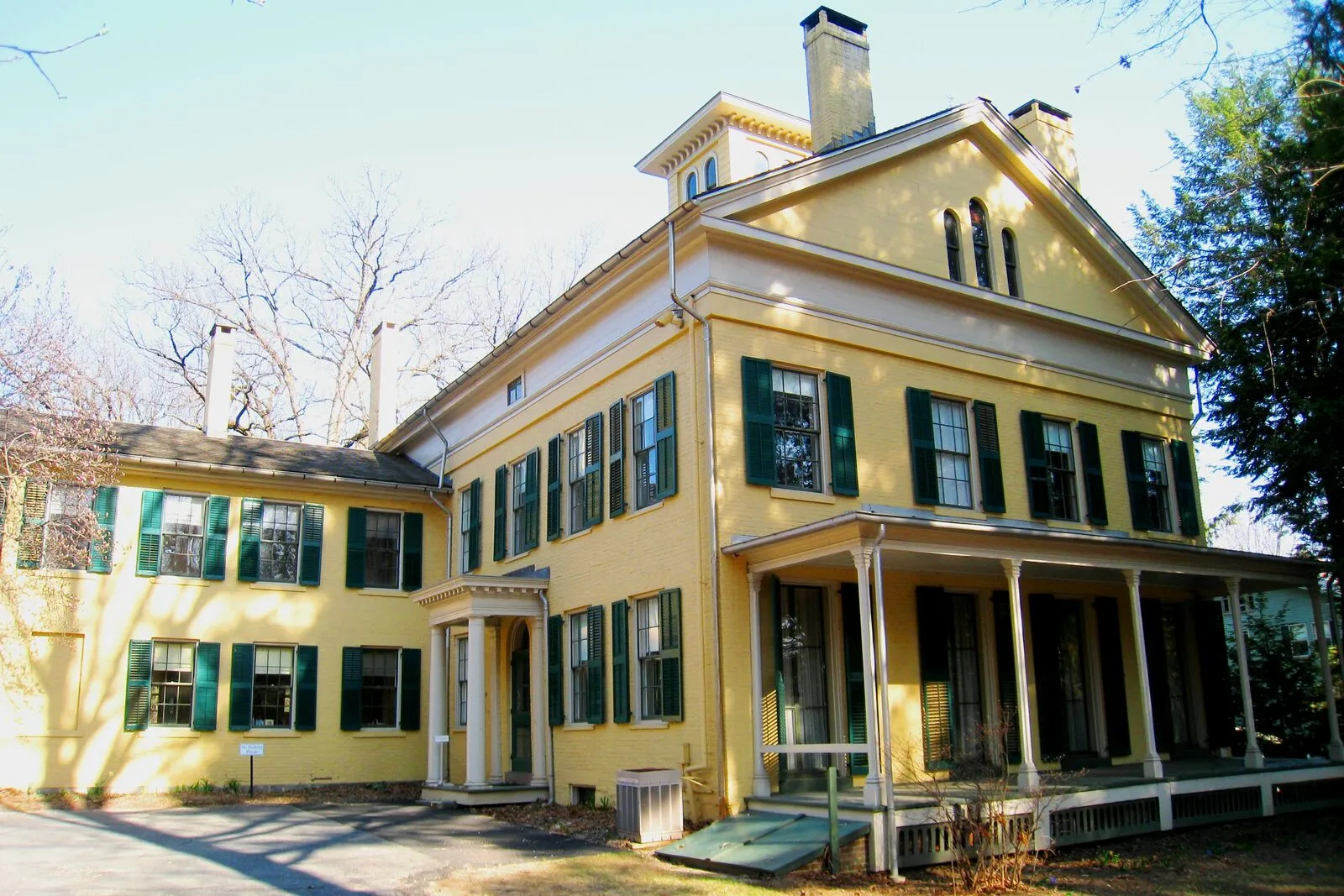 Front facade of the Emily Dickinson Homestead in Amherst: a Federal-style brick house painted ochre yellow, framed by mature trees and a white picket fence.